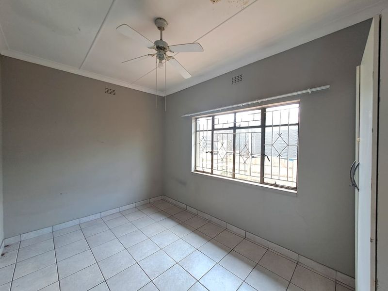 An empty bedroom featuring tiled flooring, a ceiling fan, and security bars on the window. The room requires minor cosmetic updates.