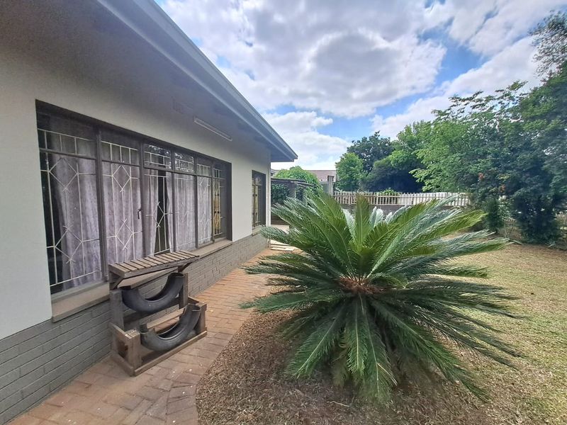 A view of the rear exterior of the house featuring brick paving, established garden landscaping, and security bars on the windows.