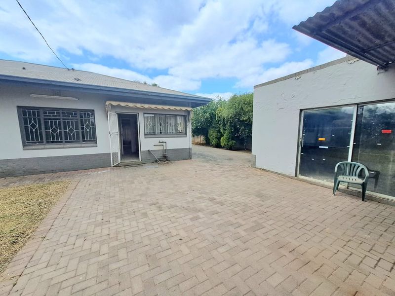 A paved rear courtyard area featuring a main house structure with security bars and an adjacent outbuilding with a sliding glass door.