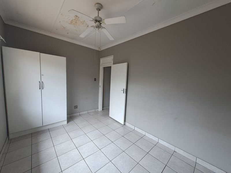 A vacant bedroom featuring tiled flooring, a built-in wardrobe, and a ceiling fan, requiring maintenance to address visible ceiling water damage.