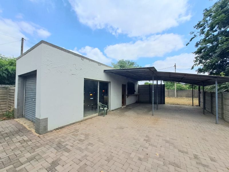 Rear exterior view featuring a paved area, covered patio space, roller shutter garage door, and sliding glass door access.