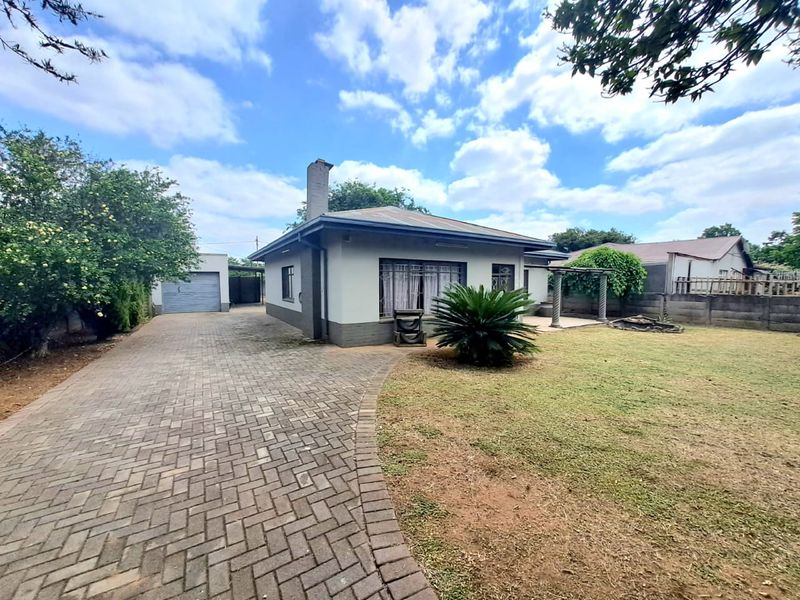 Rear view of the property featuring a paved driveway, detached garage, covered patio area, and a spacious garden with perimeter walling.