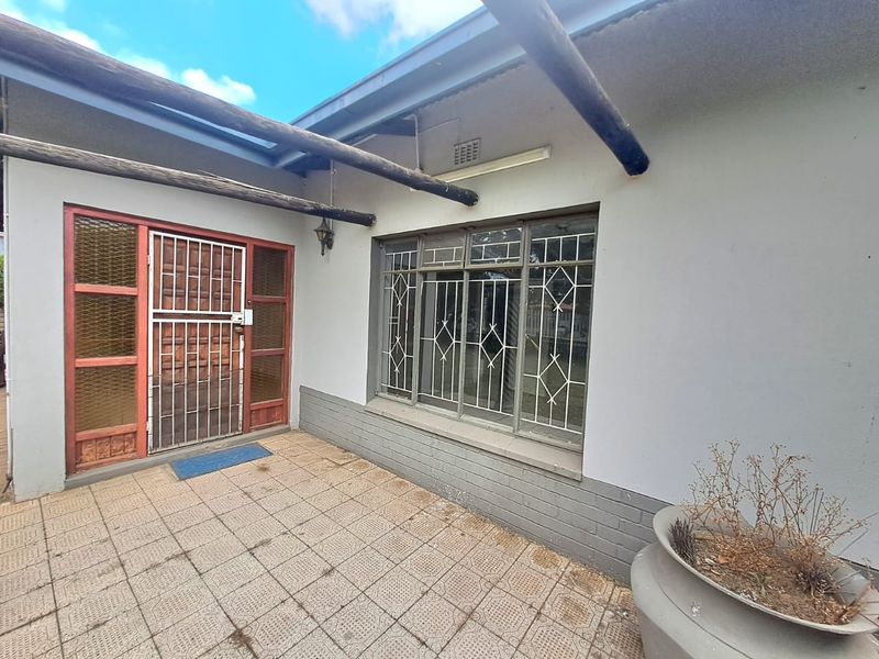 A covered patio area featuring tiled flooring, a timber pergola structure, and security-fitted doors and windows.