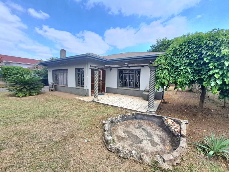 Rear view of a single-story house featuring a tiled patio with decorative columns, a pergola, and a spacious garden area.