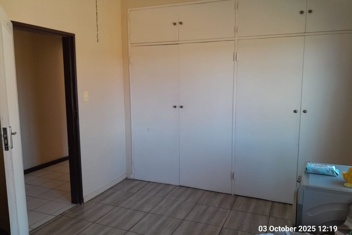 A bedroom featuring built-in floor-to-ceiling cupboards and tiled flooring, with an adjacent doorway leading to a tiled hallway.