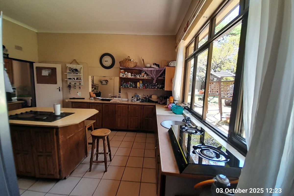 A functional kitchen featuring wooden cabinetry, a central island with a built-in hob, tiled flooring, and large windows overlooking the garden.