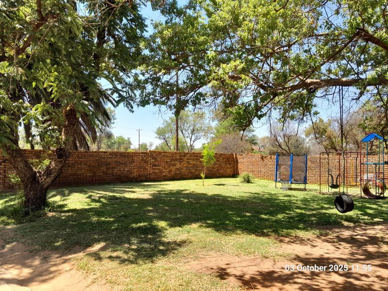 A spacious, tree-shaded garden area featuring a perimeter brick boundary wall, providing a private and established outdoor space.