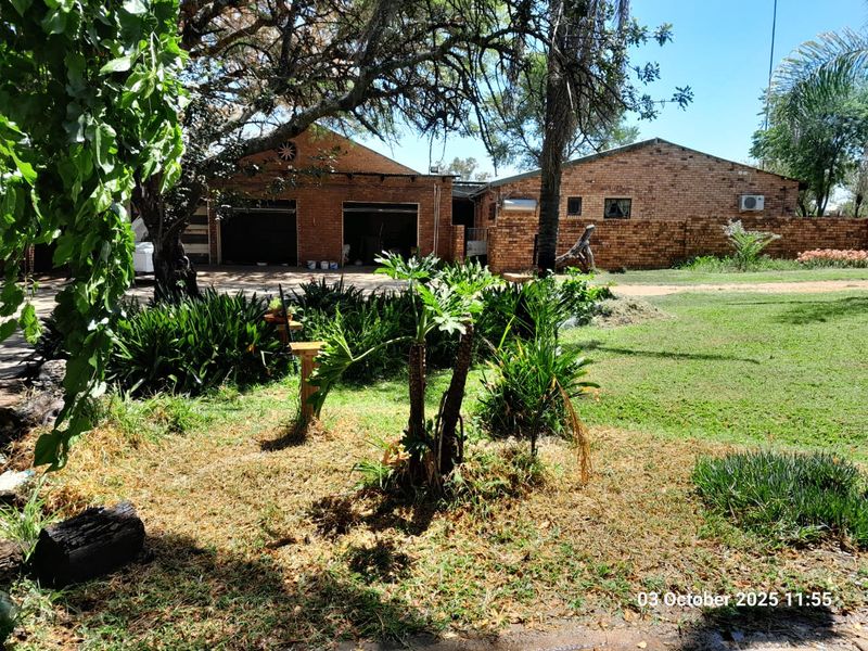 Exterior view of a brick farm building featuring multiple garage bays and a surrounding garden area with mature trees.