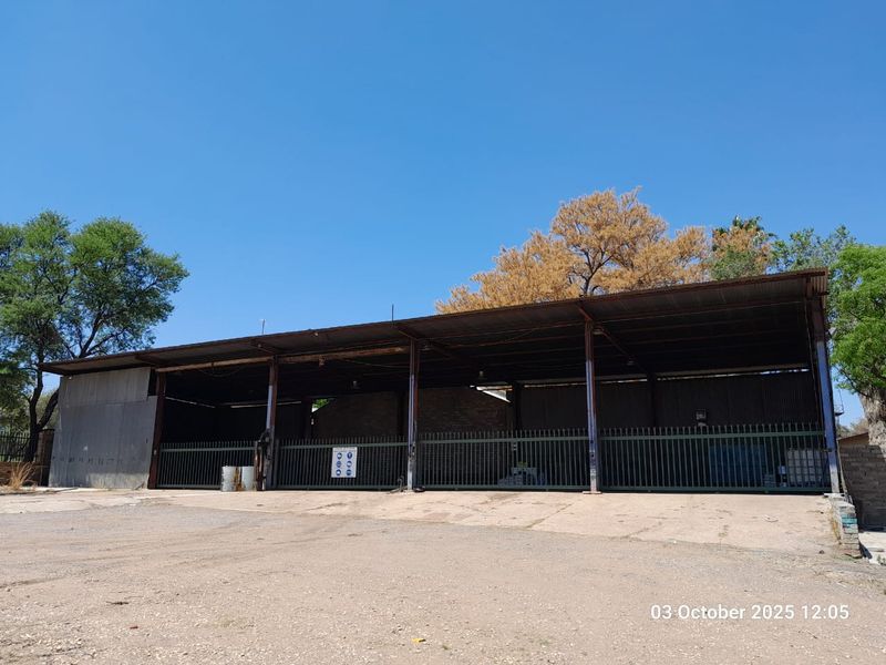 A large, open-sided farm utility shed featuring a corrugated metal roof, steel support structure, and perimeter security fencing on a concrete base.