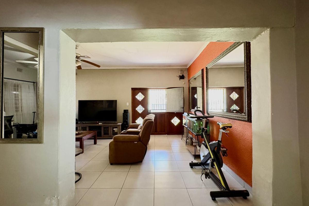 A view into a living area featuring tiled flooring, a ceiling fan, and a wooden entrance door with decorative glass panels.