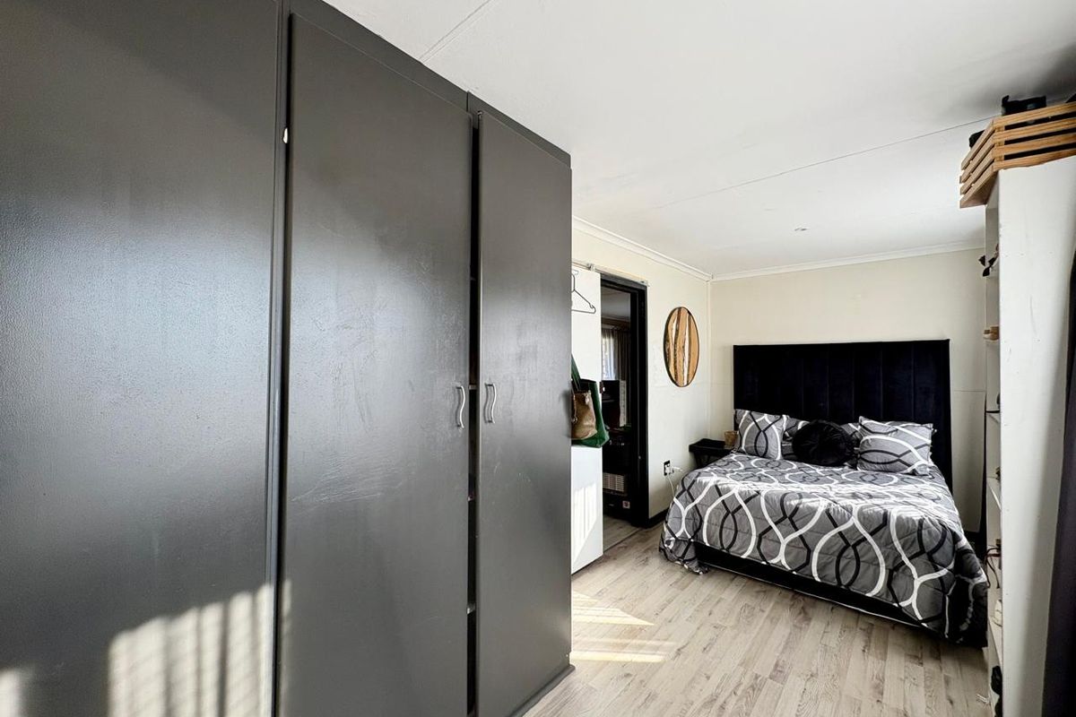 A bedroom featuring light wood-look flooring and a large dark grey built-in wardrobe.