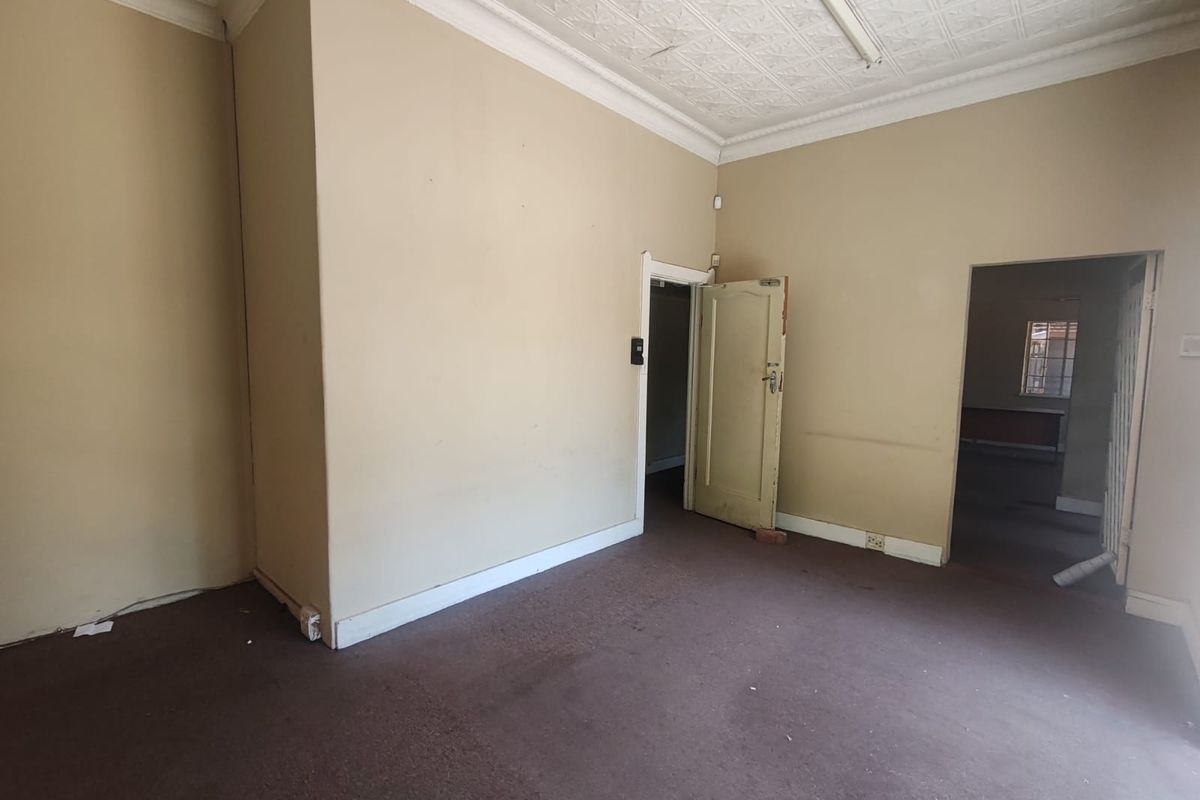 An empty living room featuring high ceilings with decorative molding, carpeted flooring, and access to adjacent rooms.