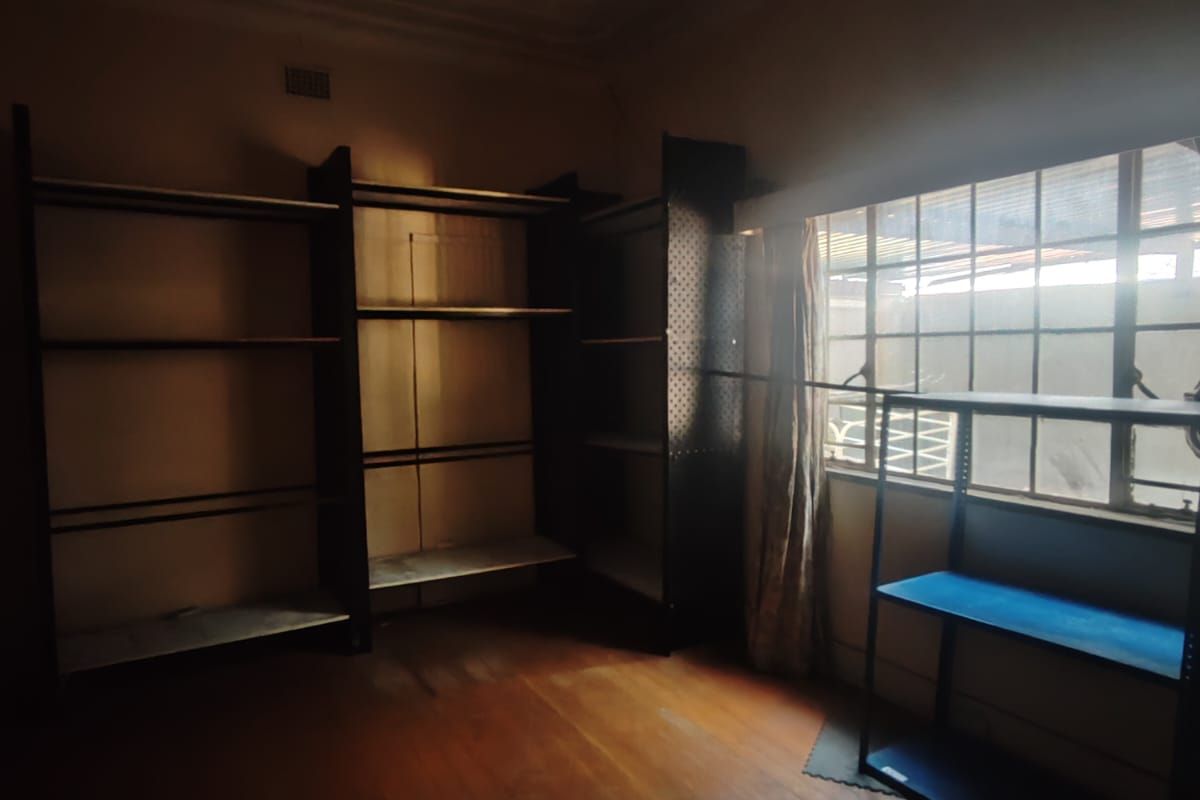 A dimly lit room featuring original timber flooring and decorative ceiling detailing, currently utilized with built-in shelving units.