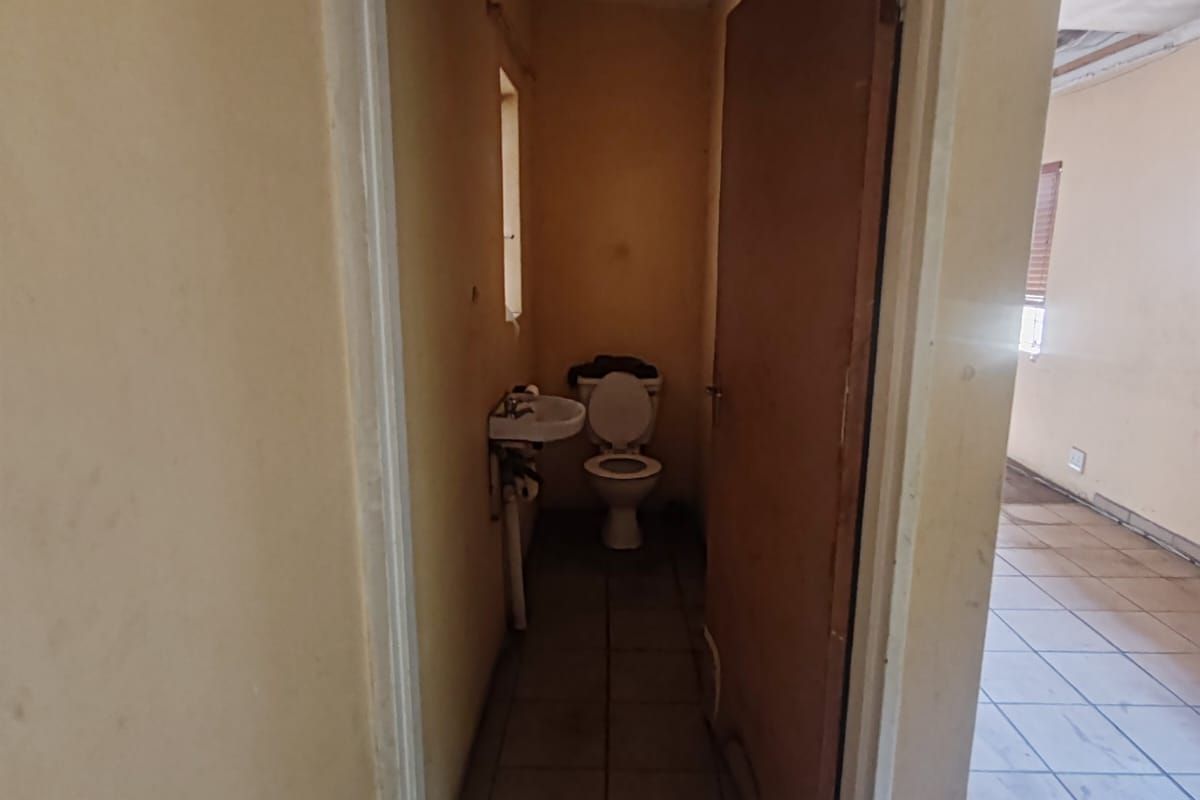 A small, dated bathroom featuring a standard toilet and wall-mounted basin, requiring significant cosmetic updates and maintenance.