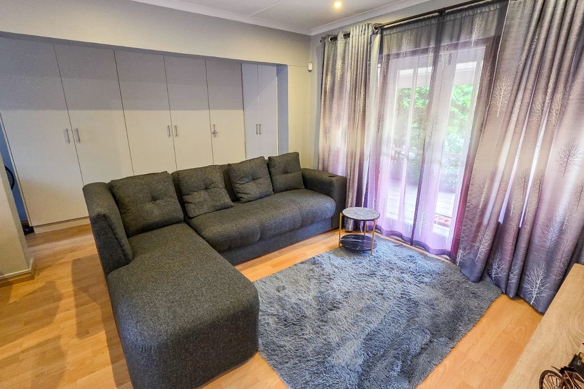 A comfortable living room featuring light laminate flooring, ample built-in storage cupboards, and a sliding glass door providing access to the outdoor area.