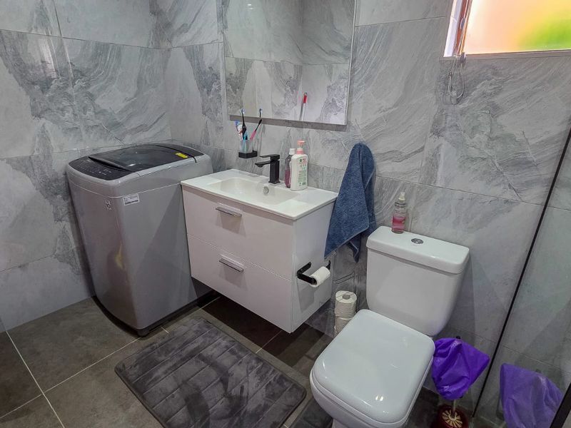 Modern bathroom featuring grey marble-effect wall tiles, a wall-mounted vanity unit, a toilet, and a glass shower enclosure.