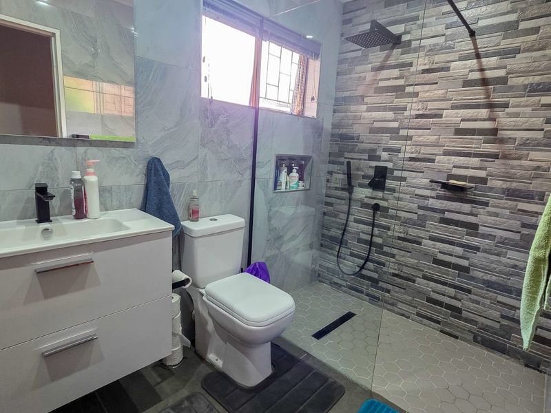 Modern bathroom featuring a vanity cabinet, toilet, and a spacious walk-in shower with a rain shower head and decorative stone-look tiled feature wall.