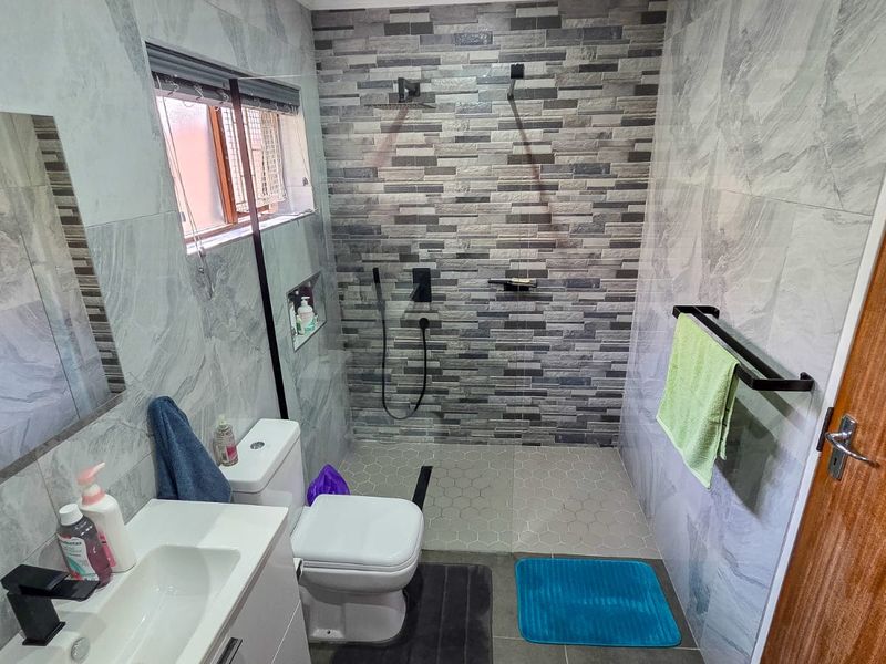 Modern bathroom featuring a walk-in shower with stone-look feature tiling, a sleek vanity unit, and contemporary black fixtures.