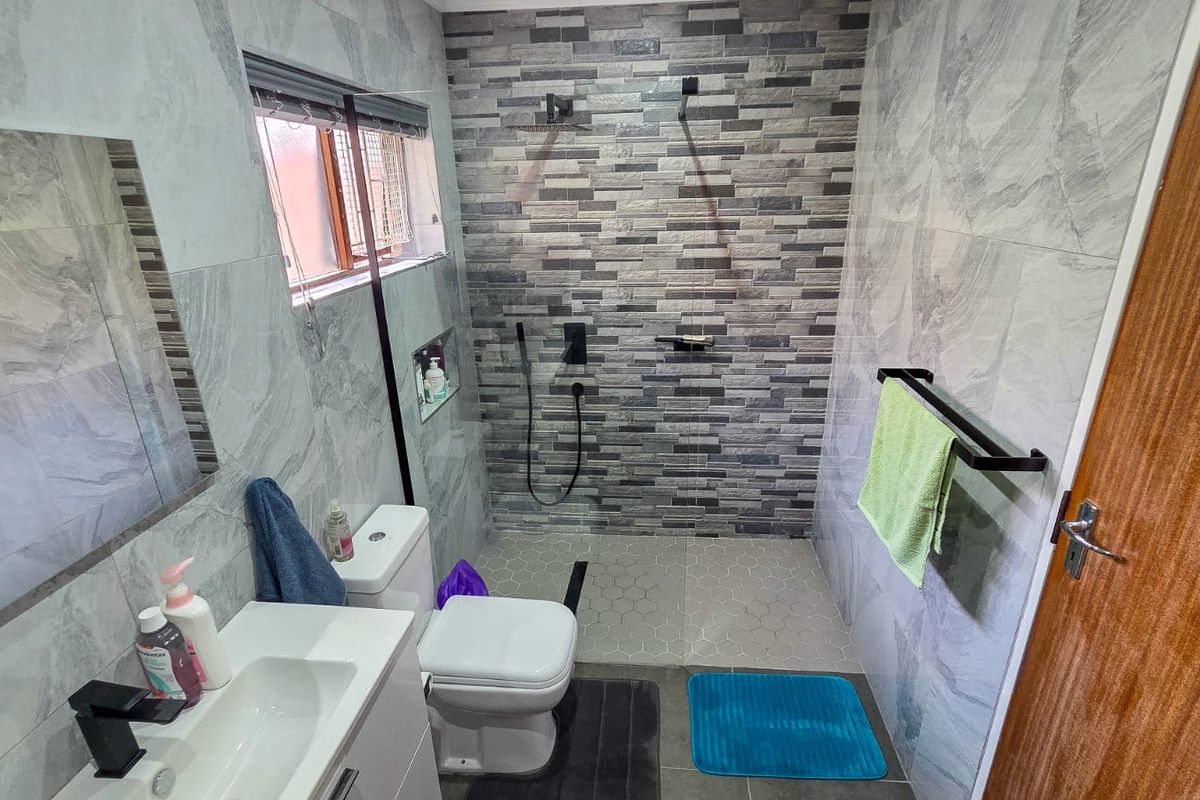 Modern bathroom featuring a walk-in shower with stone-look feature tiling, a sleek vanity unit, and contemporary black fixtures.