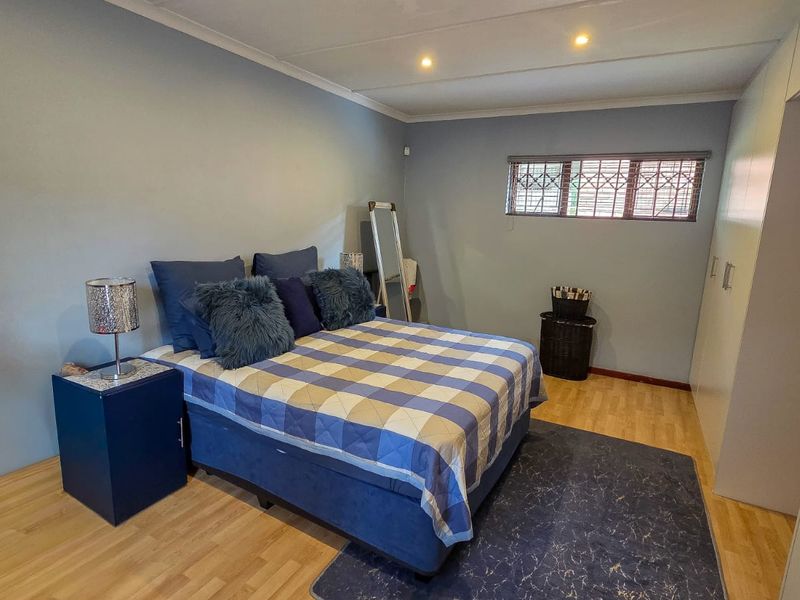 A bedroom featuring laminate flooring, built-in cupboards, and recessed downlighting, with security bars installed on the window.