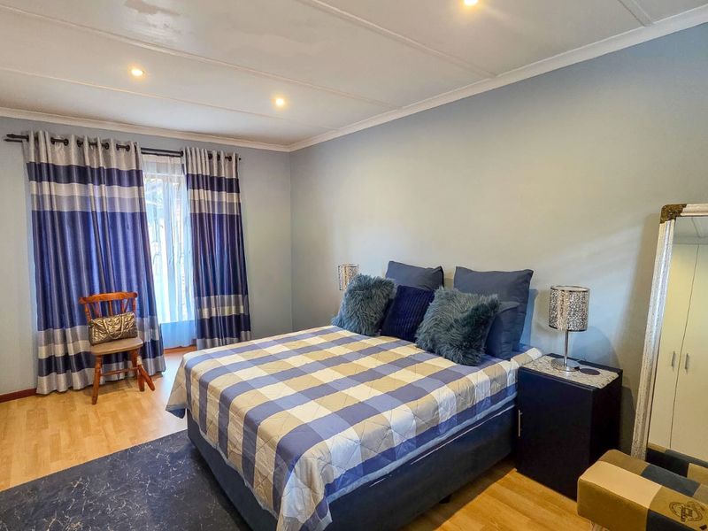A well-lit bedroom featuring laminate flooring, built-in cupboards, and recessed ceiling lighting, offering a comfortable and functional living space.