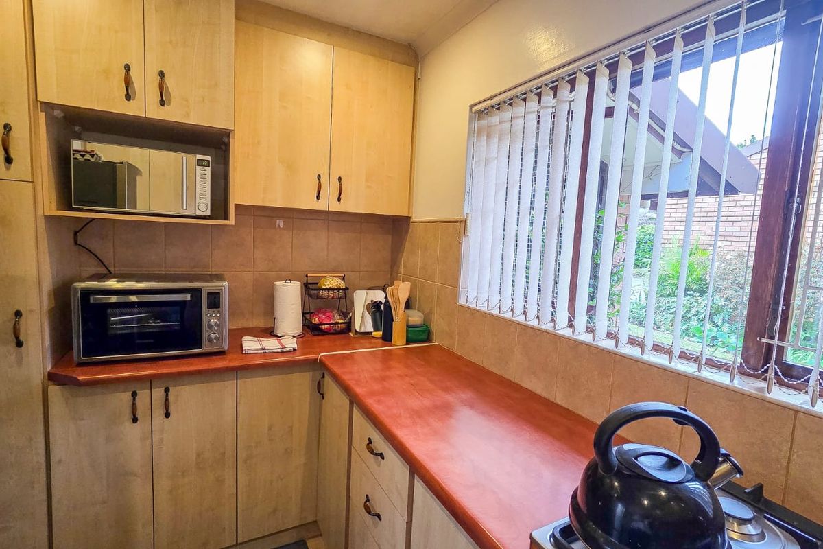 A functional kitchen featuring light wood-tone cabinetry, laminate countertops, tiled backsplash, and a built-in microwave, with a window overlooking the garden.