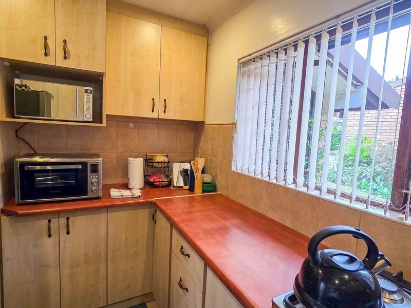A functional kitchen featuring light wood-tone cabinetry, laminate countertops, tiled backsplash, and a built-in microwave, with a window overlooking the garden.