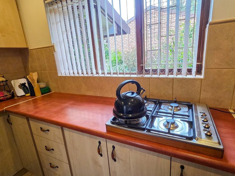 A functional kitchen area featuring built-in cabinetry, a gas hob, and tiled backsplash, offering a practical workspace with natural light from the window.