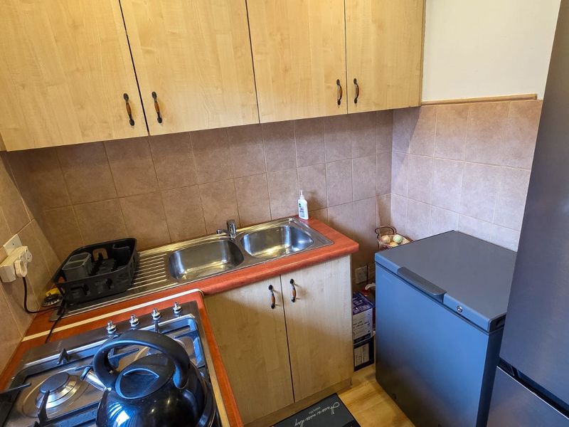 A functional kitchen featuring light wood-finish cabinetry, a double stainless steel sink, tiled backsplash, and a built-in gas hob.