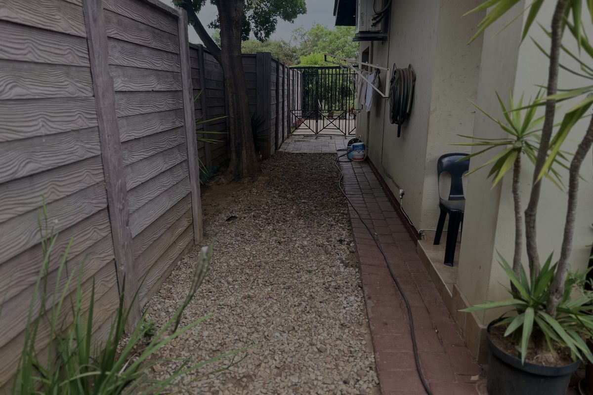 A side exterior walkway featuring a gravel path, paved border, and secure metal gate access.