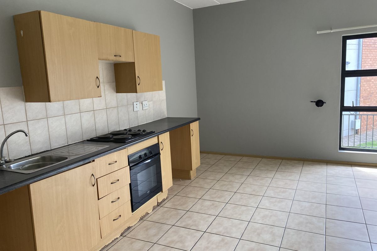 A functional kitchen featuring light wood cabinetry, tiled splashbacks, a built-in oven and hob, and tiled flooring in an open-plan layout.