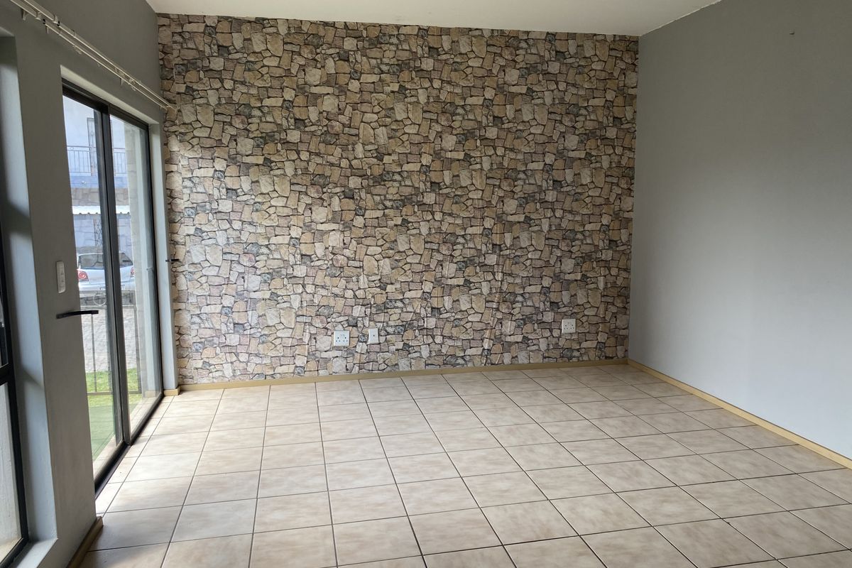 An empty living area featuring tiled flooring, a stone-effect feature wall, and large sliding glass doors providing natural light and outdoor access.