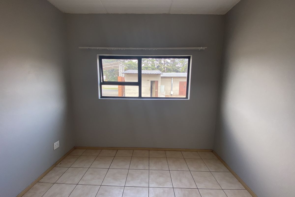 A vacant bedroom featuring neutral grey walls, tiled flooring, and a dark-framed window providing natural light.