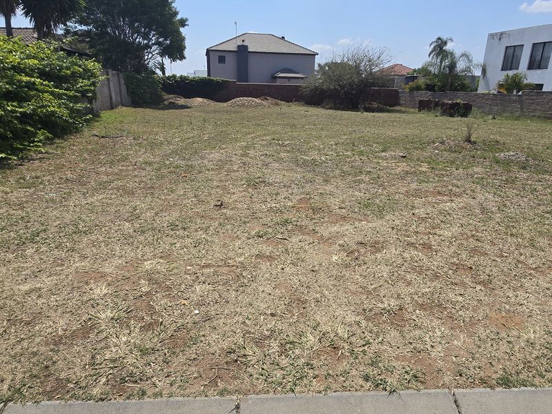 A vacant residential plot of land featuring perimeter boundary walls and established greenery, offering a clear space for future development.