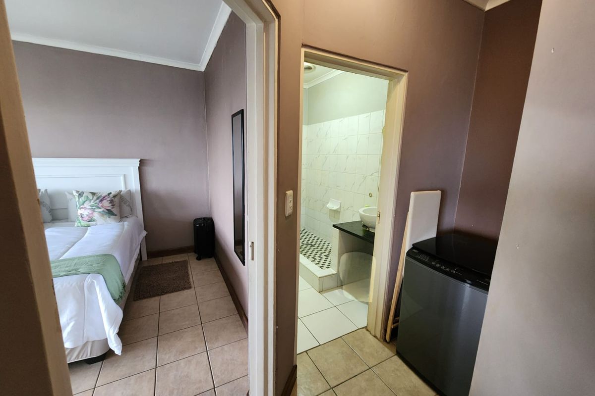 A bedroom featuring tiled flooring and coving, with an adjoining en-suite bathroom equipped with a shower and vanity basin.