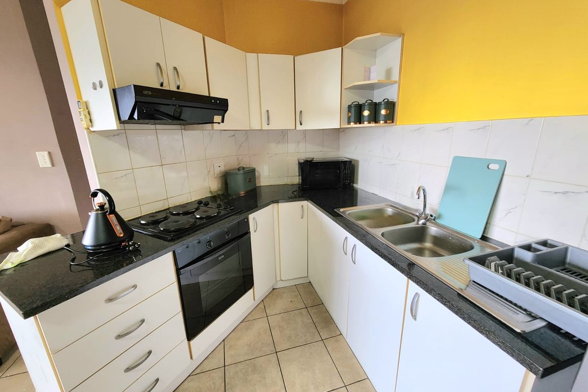 Functional kitchen featuring white cabinetry, granite countertops, built-in oven, electric hob, extractor fan, and a double bowl sink with tiled backsplash.