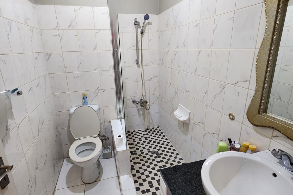 Compact bathroom featuring a walk-in shower, toilet, and a granite-topped vanity basin with tiled walls and flooring.