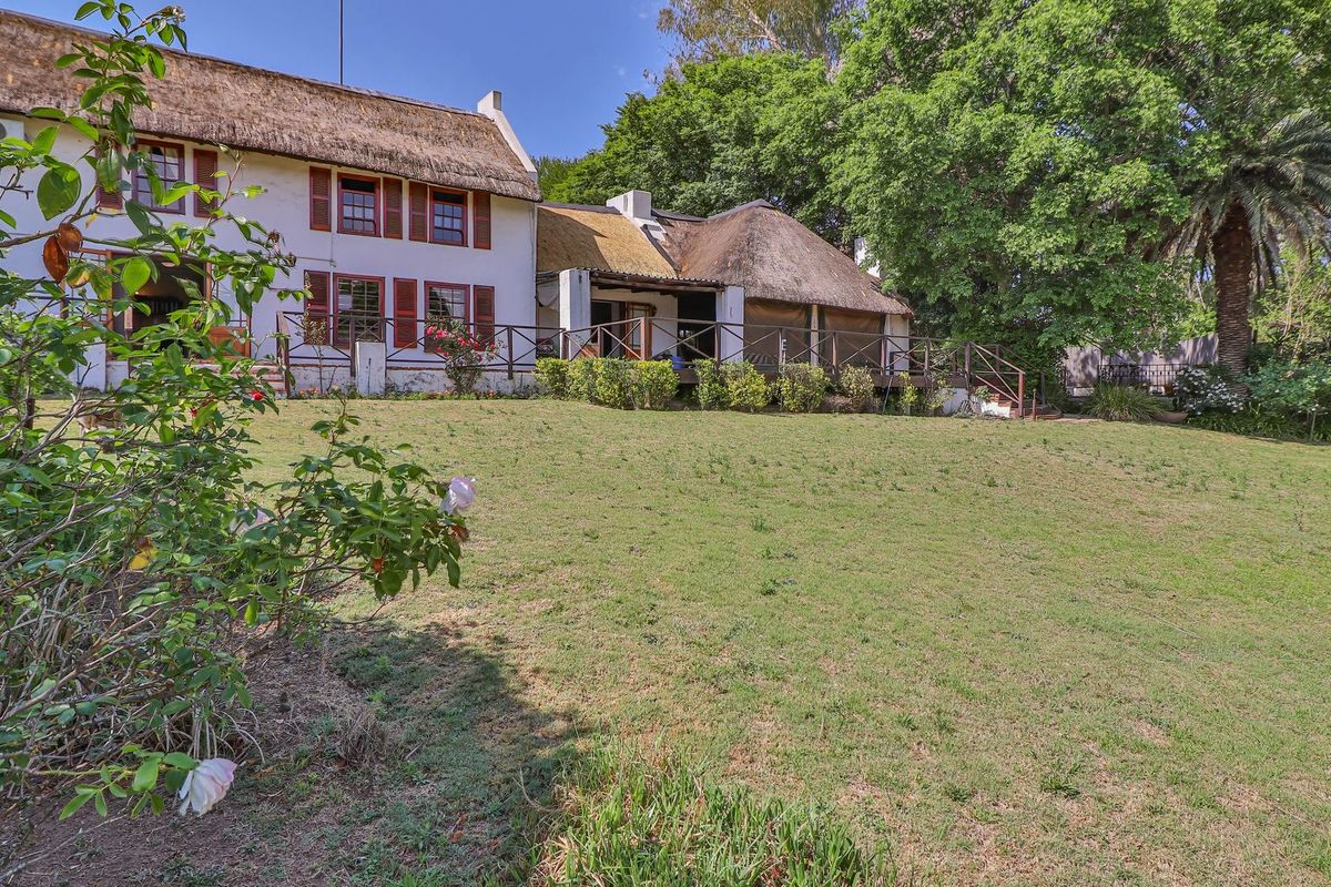 A view of the rear elevation of a traditional thatched-roof farmhouse, featuring a raised wooden deck and expansive garden area.