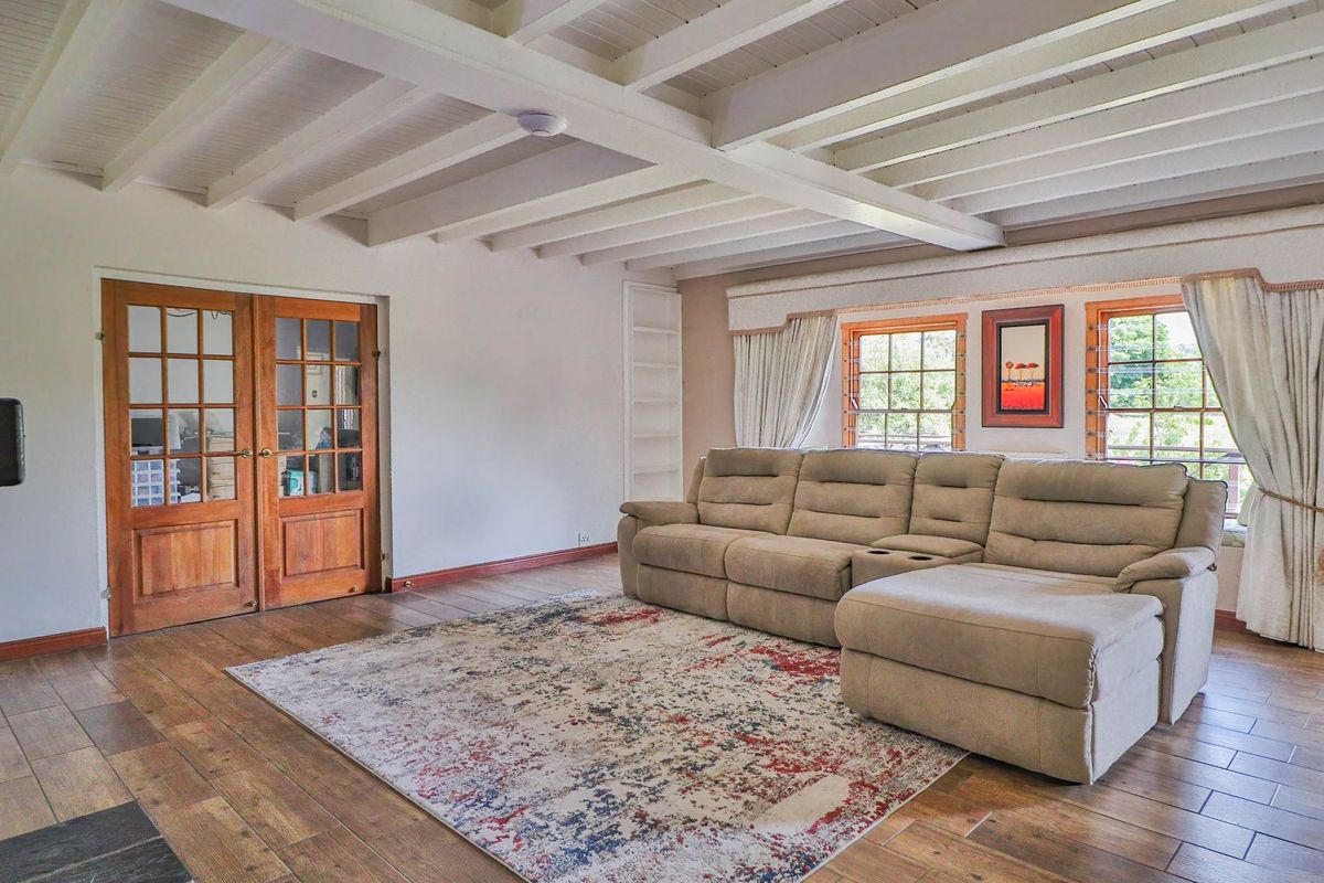 Spacious living room featuring exposed white timber ceiling beams, wood-look tiled flooring, and double wooden doors leading to an adjacent room.