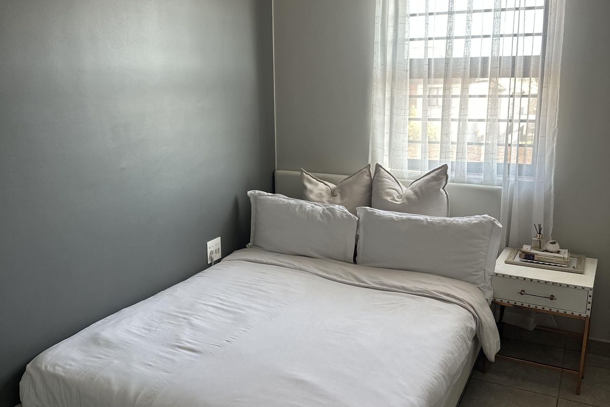 A well-maintained bedroom featuring neutral grey walls, tiled flooring, and a window fitted with security bars.