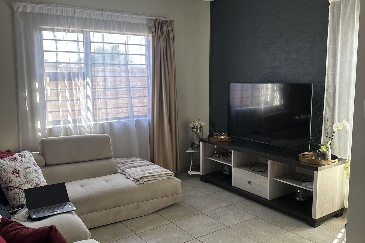 A comfortable living room featuring tiled flooring, a dark accent wall, and large windows with security bars, providing a functional and well-lit space.