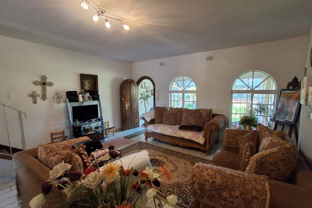 Spacious living room featuring arched windows, tiled flooring, and a classic arched wooden door, providing a bright and traditional living space.