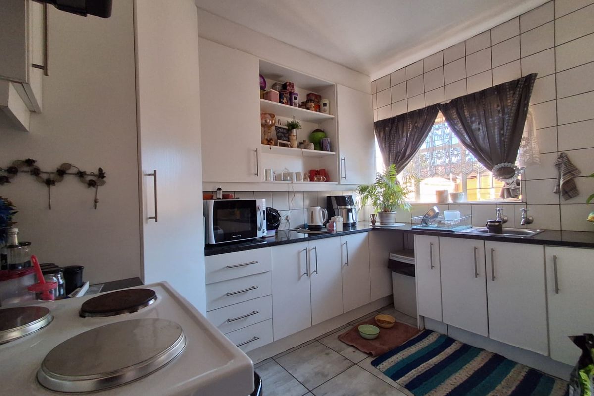 A functional kitchen featuring white cabinetry, dark countertops, tiled splashbacks, and a built-in stove, offering a practical layout for daily meal preparation.
