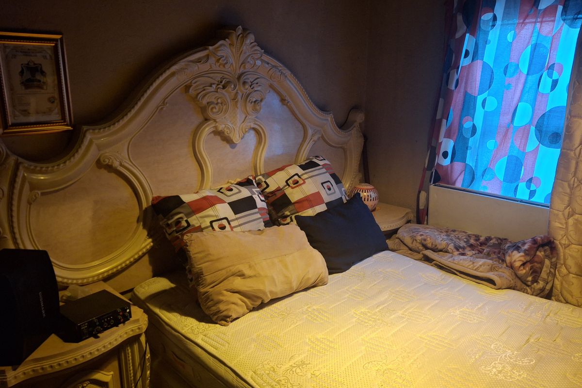 A bedroom featuring a decorative built-in headboard and a window with patterned curtains, providing a cozy sleeping space.