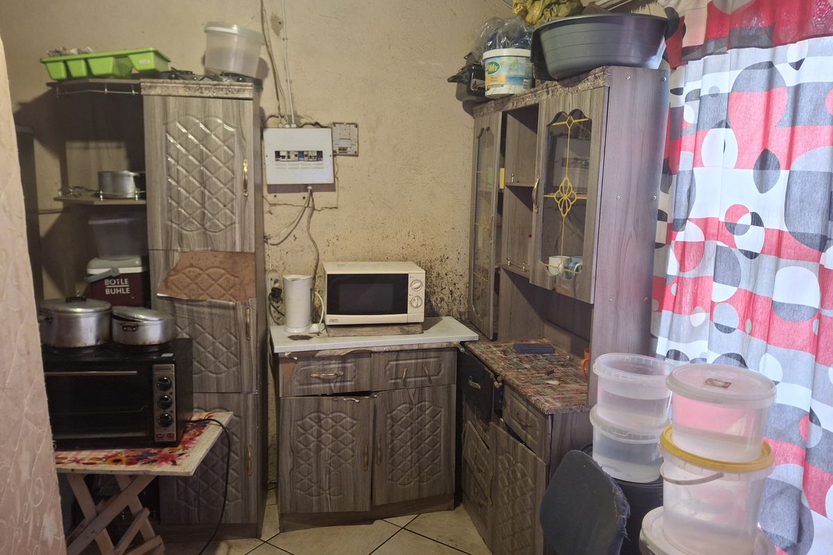 A compact kitchen area featuring built-in cabinetry, tiled flooring, and visible electrical infrastructure, requiring significant maintenance and cosmetic updates.