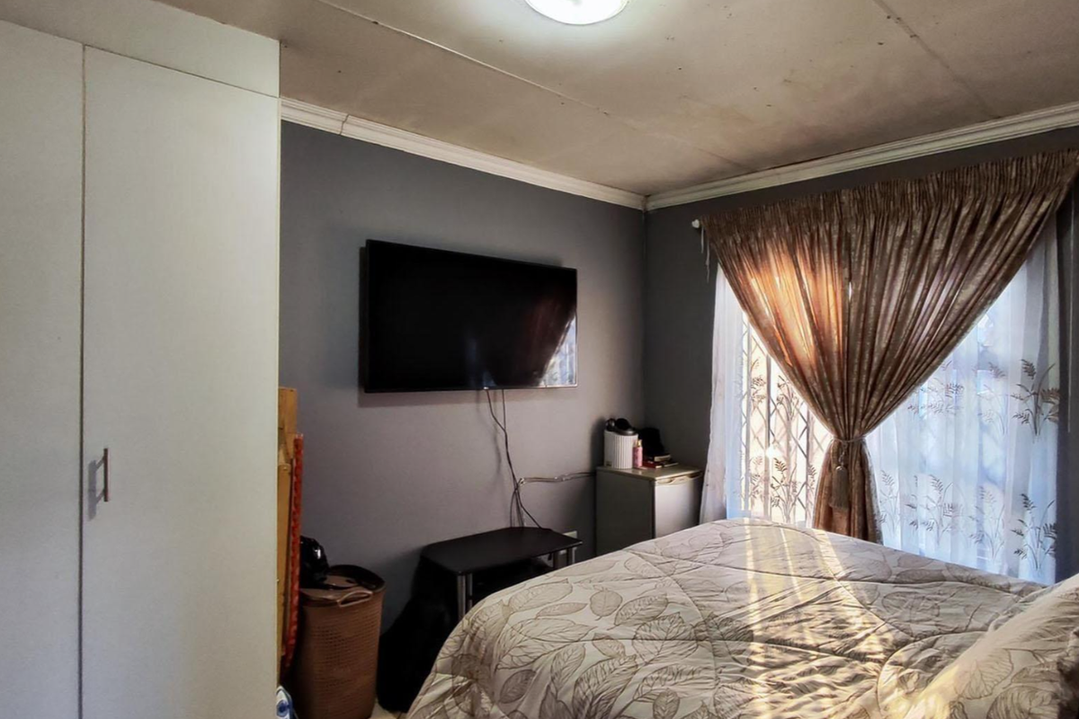 A bedroom featuring built-in wardrobe cabinetry, a wall-mounted television, and a window with security bars.