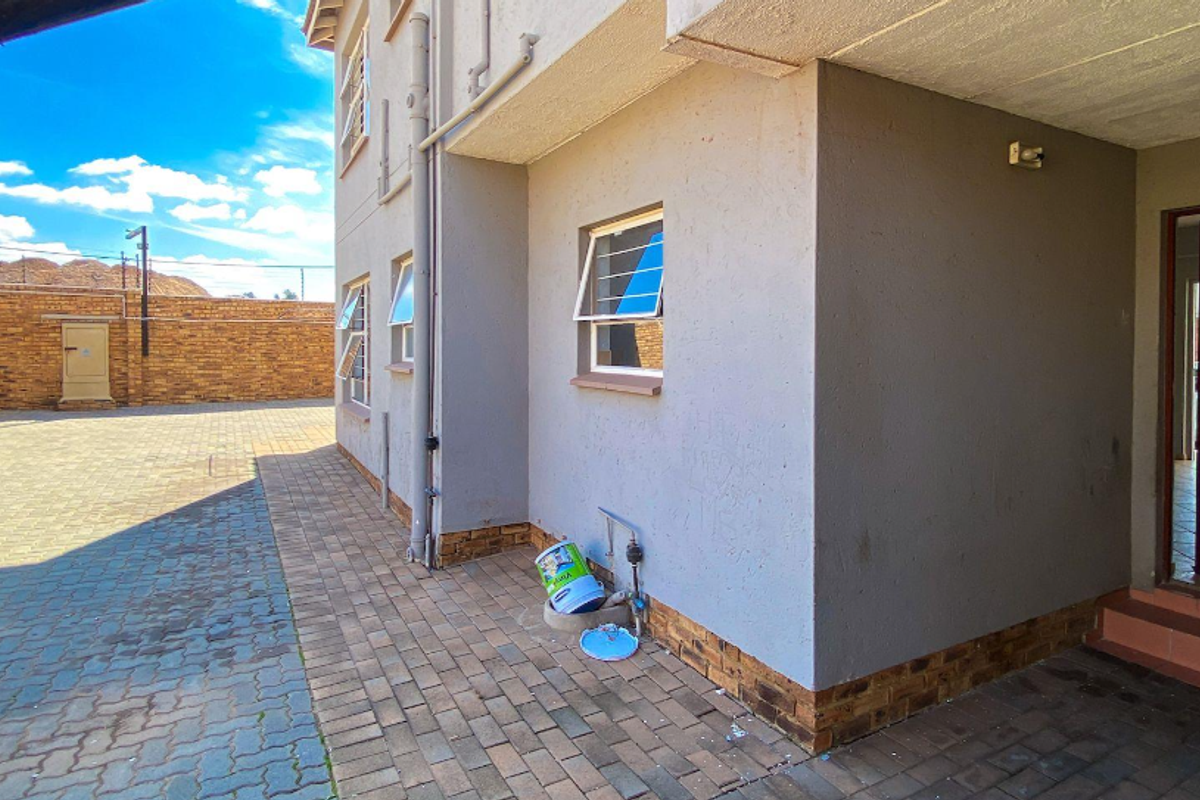 Exterior view of the apartment building featuring paved driveway, brick boundary wall, and private entrance with tiled steps.
