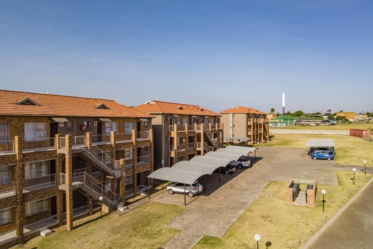 Aerial view of a multi-story apartment complex featuring brick facades, tiled roofs, external staircases, and covered parking bays within a landscaped estate.