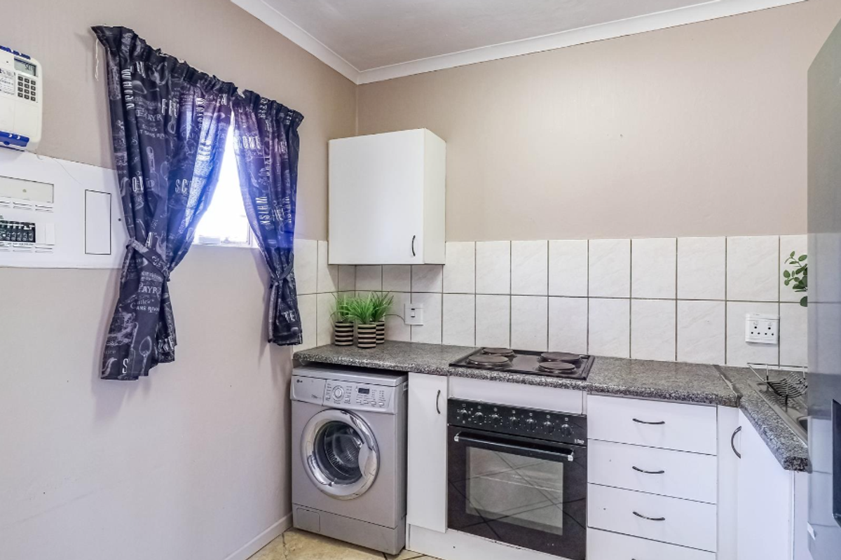 Compact kitchen featuring built-in cabinetry, granite-look countertops, integrated oven and hob, and dedicated space for a washing machine.