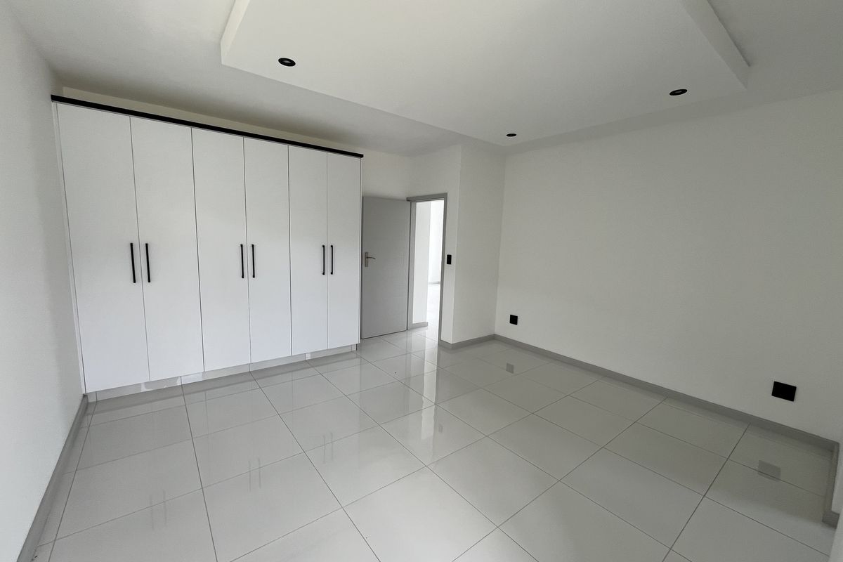 A bright, modern bedroom featuring large white built-in wardrobes, polished porcelain floor tiles, and a recessed ceiling design with integrated downlights.